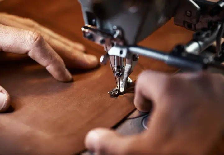 Manos cosiendo con precisión una pieza de cuero vegetal en una máquina de coser industrial.