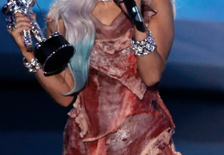 Lady Gaga con su icónico vestido de carne, sosteniendo un premio.