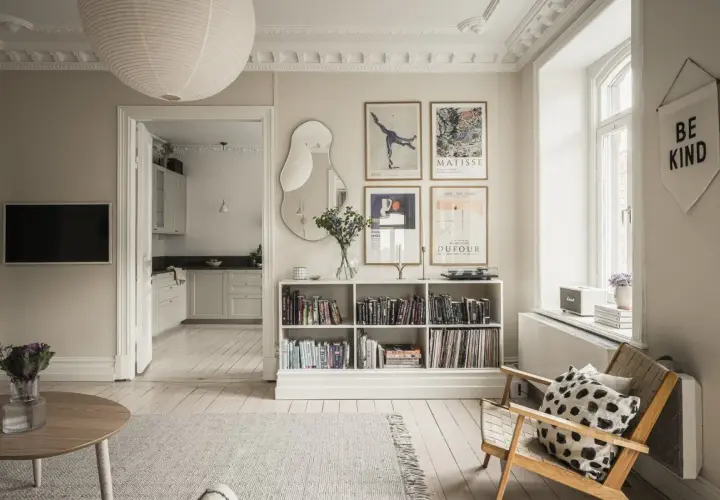 Salón con estilo de Estocolmo: estanterías blancas llenas de libros, arte en las paredes, silla de madera y alfombra gris.