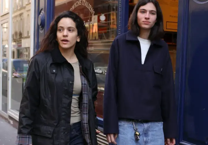 Dos jóvenes pasean por una calle, uno con chaqueta negra y el otro con jersey azul marino. Quizás buscando la loli bahía.