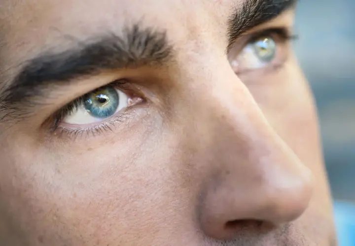 Primer plano de los ojos de un hombre, destacando sus cejas pobladas y el iris azul verdoso.