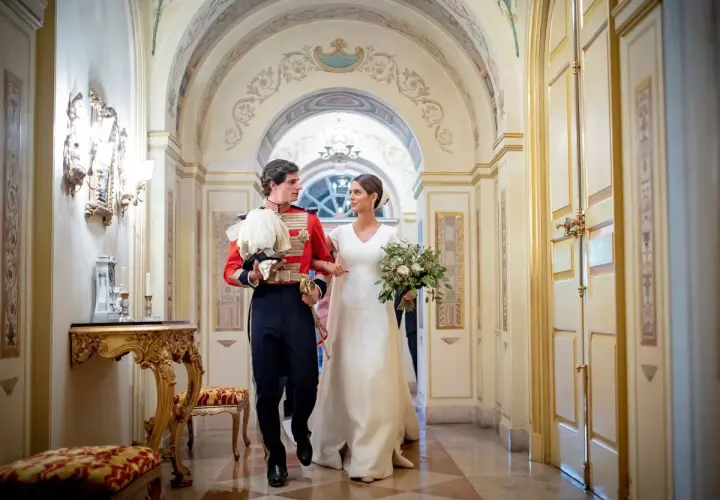Sofía Palazuelo y su esposo, con traje de gala, caminan por un pasillo adornado, celebrando su boda.