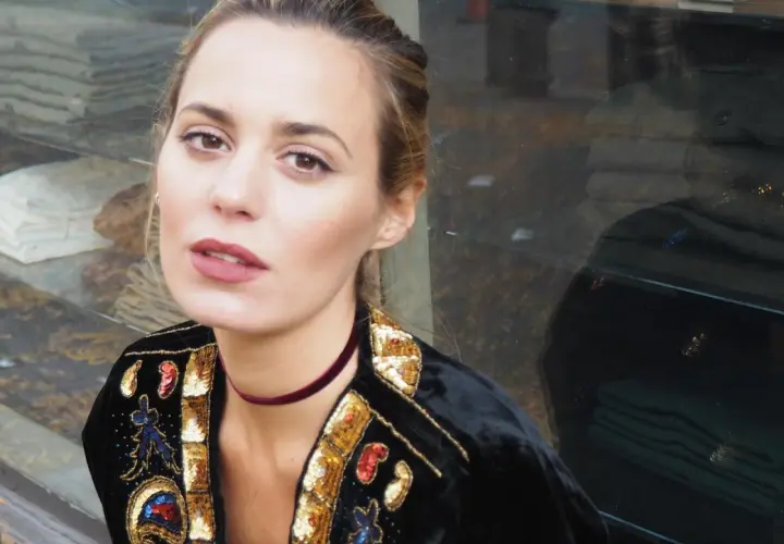 Claudia Ortiz Domecq, con un choker de terciopelo y chaqueta bordada, posa con mirada intensa frente a un escaparate.