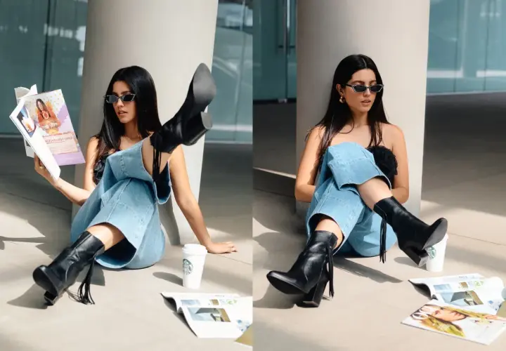 Chica con gafas de sol y jeans anchos, luciendo unas **botas en verano** mientras lee una revista junto a un café.