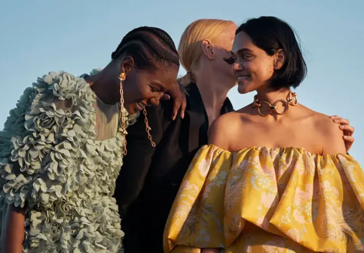 Tres mujeres ríen, una con un vestido verde con flores, otra con un collar dorado y un vestido amarillo estampado. Moda ecofriendly que es.