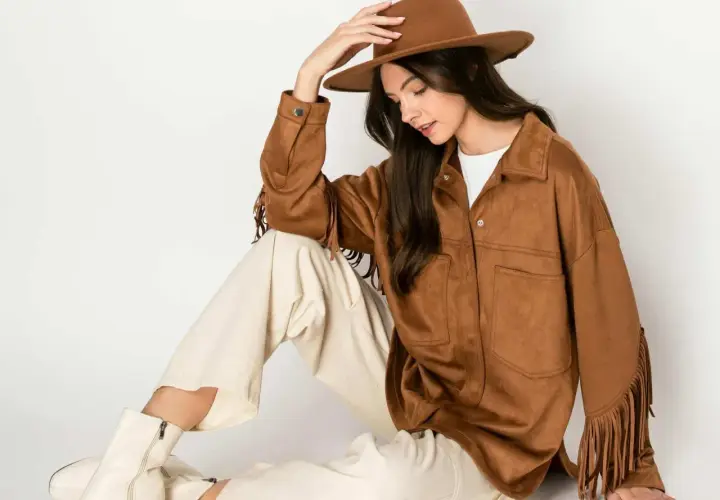 Mujer con sombrero y chaqueta de serraje que es suave y con flecos. Pantalones crema y botas blancas completan el look.