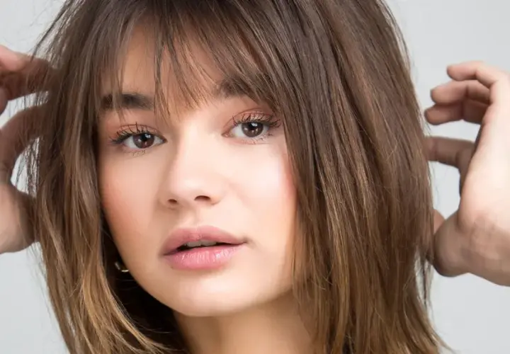 Chica con flequillo desfilado y cabello castaño, ideal para cortes de pelo para cara redonda.
