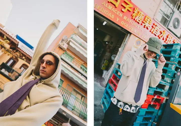 Ralphie Choo, con sudadera y corbata, posa con estilo urbano frente a un almacén.