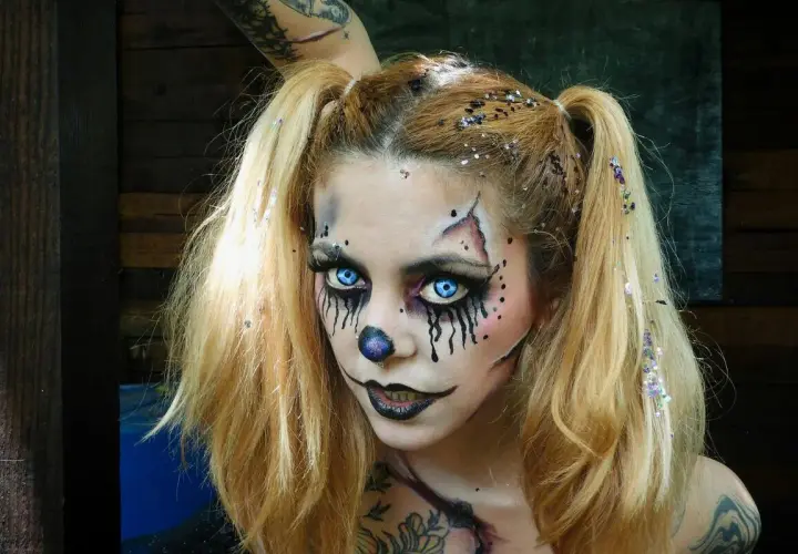 Chica con maquillaje de halloween de payaso aterrador, ojos azules brillantes, nariz de payaso y purpurina en el cabello.
