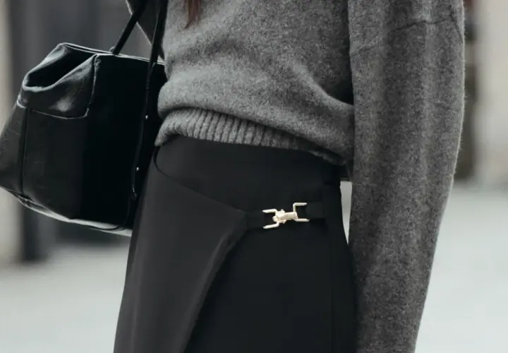 Chaqueta gris y bolso negro sobre falda negra larga con detalle dorado. Un look elegante para saber como combinar una falda negra larga.