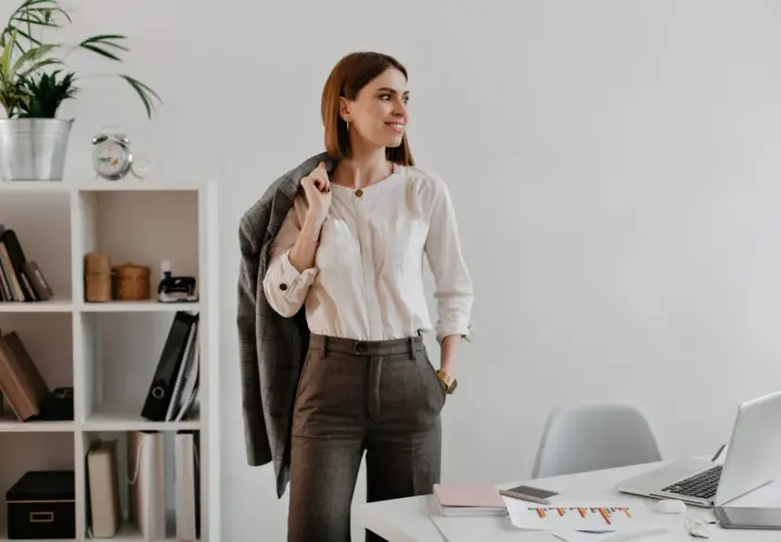 Mujer con un elegante outfit oficina: camisa blanca, pantalón gris y chaqueta a cuadros.