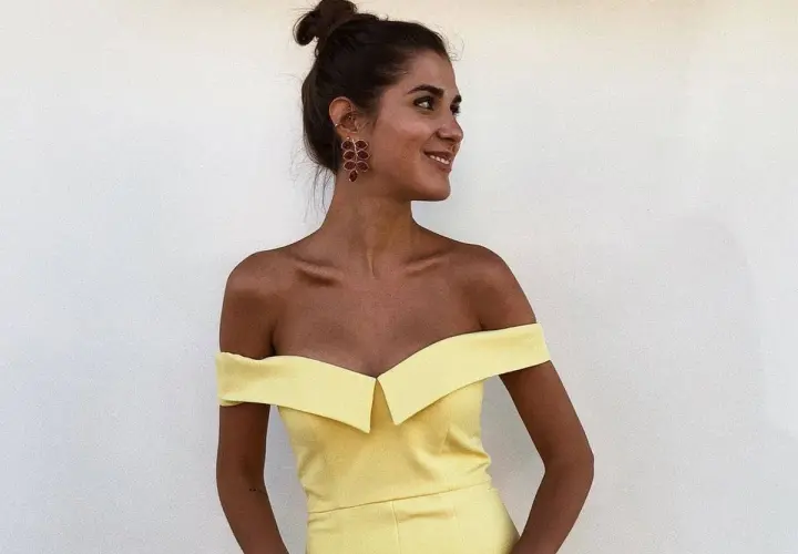 Mujer con moño alto y pendientes rojos, luciendo un vestido amarillo de hombros caídos. Ideas para combinar zapatos para vestido amarillo.