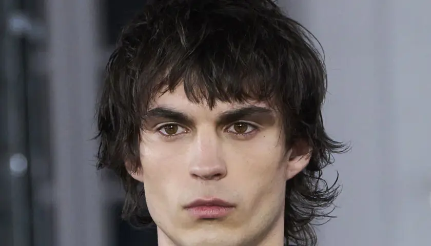 Joven con un moderno corte mullet, cabello oscuro y despeinado, mirada intensa y cejas marcadas.