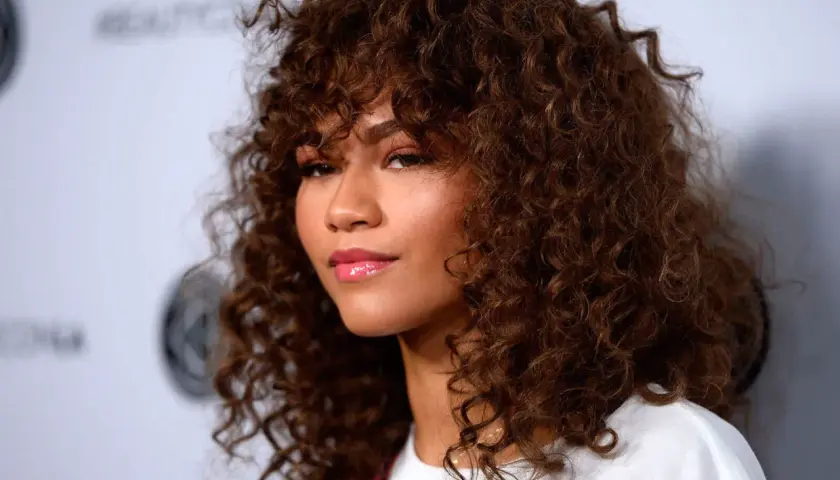 Mujer con cabello castaño rizado y flequillo, un ejemplo de cortes de pelo rizado que realzan su belleza natural.