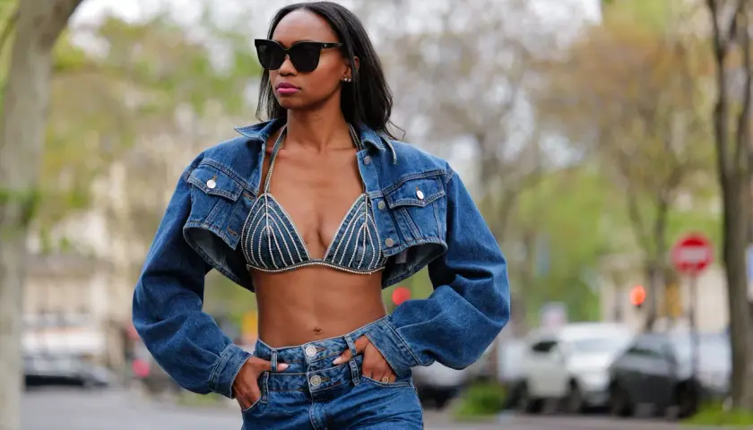 Mujer con gafas de sol luce un conjunto de **denim on denim**: chaqueta corta y sujetador de pedrería, combinados con jeans.
