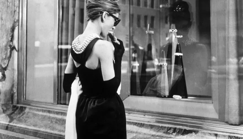 Audrey Hepburn, icónica en su vestido negro y perlas, disfruta de un pastel frente a Tiffany's.
