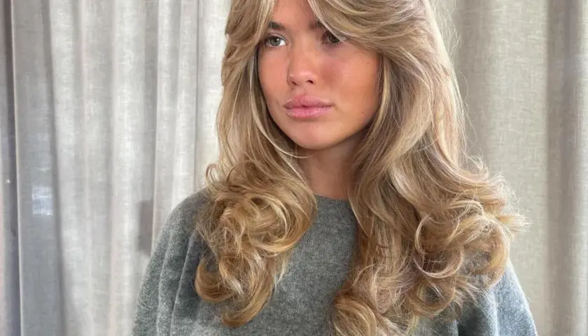 Mujer con cabello rubio y ondas voluminosas, un corte **hush cut** que enmarca su rostro.