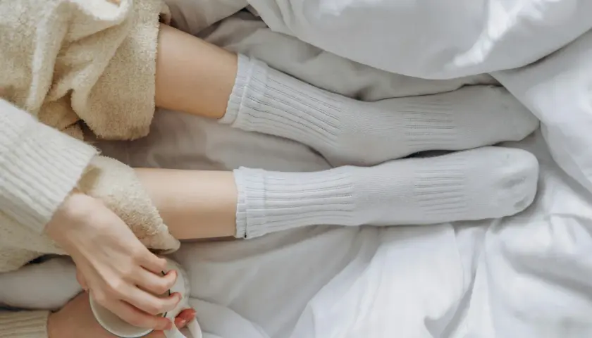 Piernas con calcetines blancos de poliamida, envueltas en mantas suaves, sosteniendo una taza.