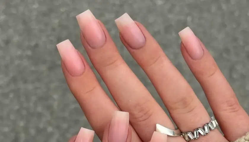 Manos con uñas naturales bonitas en forma cuadrada, con un degradado sutil de rosa pálido a transparente.
