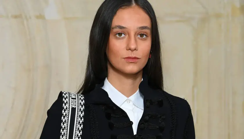 Joven con estilo cayetano, luce un blazer oscuro con detalles de pasamanería y una camisa blanca. Su bolso Dior complementa el look.