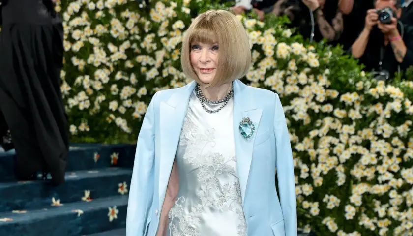 Anna Wintour, figura clave de que es la Gala Met, posa con un traje azul claro y un vestido blanco bordado, adornada con un collar y un broche de corazón.