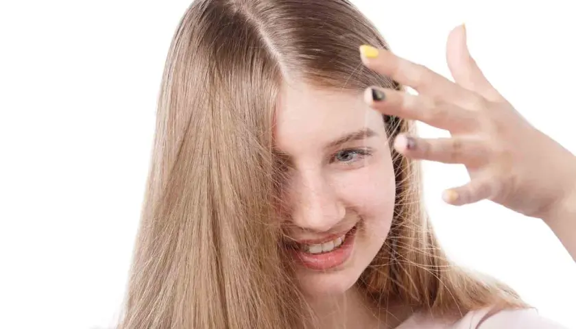 Chica sonriente con cabello rubio que se electrifica. Descubre cómo quitar la electricidad del pelo para un look suave.