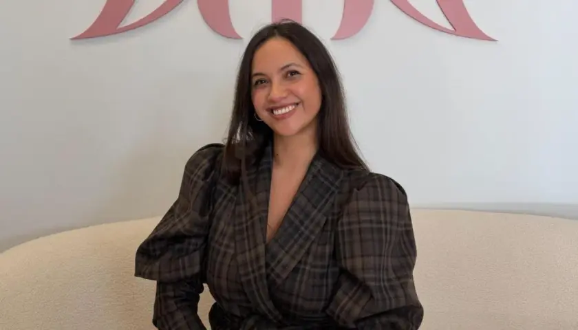 Sonriendo, una mujer con un blazer de cuadros marrones y mangas abullonadas. Sus opiniones sobre miphai son positivas.