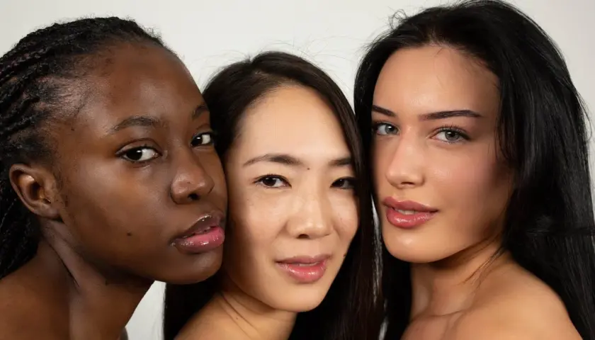 Tres mujeres de diferentes etnias, una con piel **color negro**, se miran a la cámara con labios brillantes.