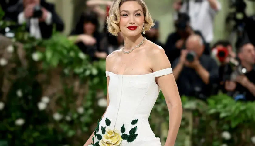 Gigi Hadid deslumbrante en la Met Gala, con un vestido blanco adornado con rosas amarillas y verdes.