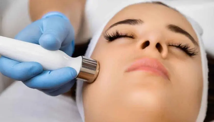 Un rostro recibe un tratamiento facial con exosomas, aplicado con un dispositivo de mano por un profesional con guantes azules.