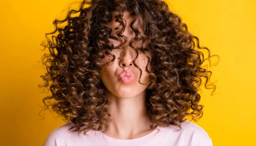 Mujer con pelo corto rizado y labios en forma de beso, sobre fondo amarillo.