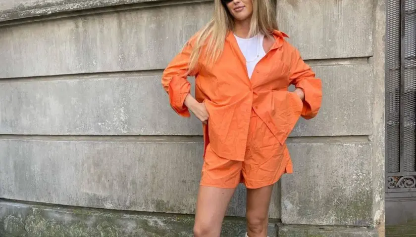 Mujer con conjunto naranja, gafas de sol y botas blancas. Se ve muy comfy y lista para pasear.