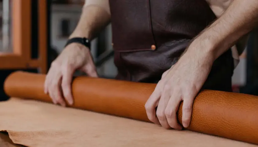 Manos de artesano desenrollando un rollo de cuero, mostrando la textura y el color natural del material. Se pregunta de que esta hecho el cuero.