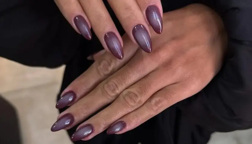 Manicura con uñas almendradas en tono morado oscuro, con un efecto degradado que recuerda a las aura nails.