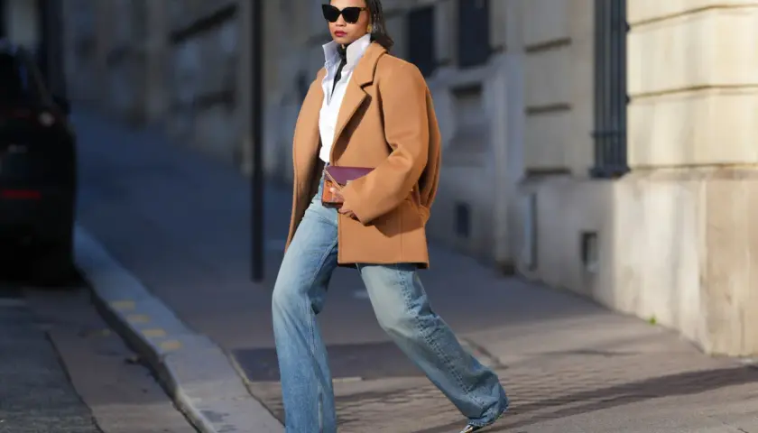 Mujer con abrigo camel, camisa blanca y jeans anchos, luciendo un bolso morado. Su estilo es muy aesthetic.