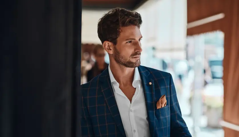 Un invitado boda hombre sin traje, con chaqueta a cuadros, camisa blanca y pañuelo naranja.