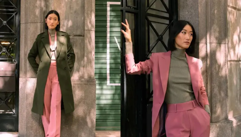 Dos mujeres posan en la calle. Una lleva un abrigo verde y pantalones rosas. La otra, un traje rosa y jersey verde. El verde y negro combinan con el entorno urbano.