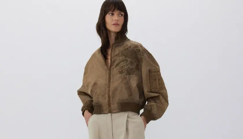 Mujer posando con una bomber marrón con bordado floral. Ideal para combinar bomber mujer con estilo casual.