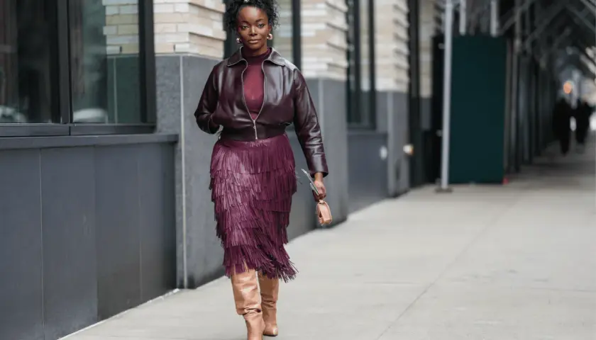 Mujer con falda de flecos burdeos y chaqueta a juego, luciendo botas altas. Un ejemplo de cómo combinar zapatos burdeos mujer con estilo.