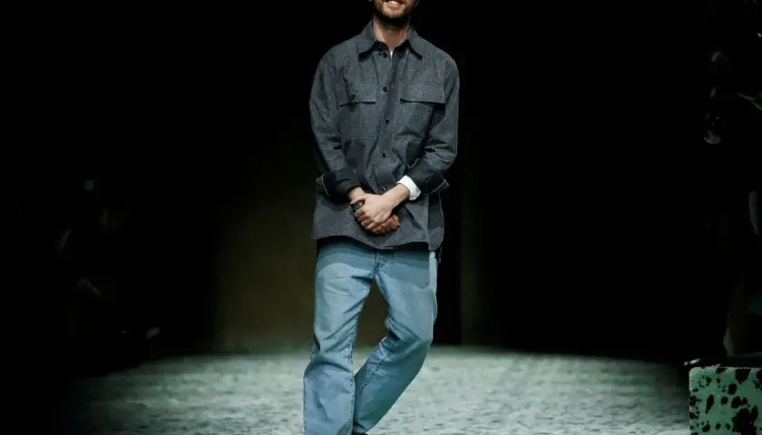 Matthieu Blazy, diseñador de Bottega Veneta, sonríe en la pasarela con camisa gris y vaqueros.