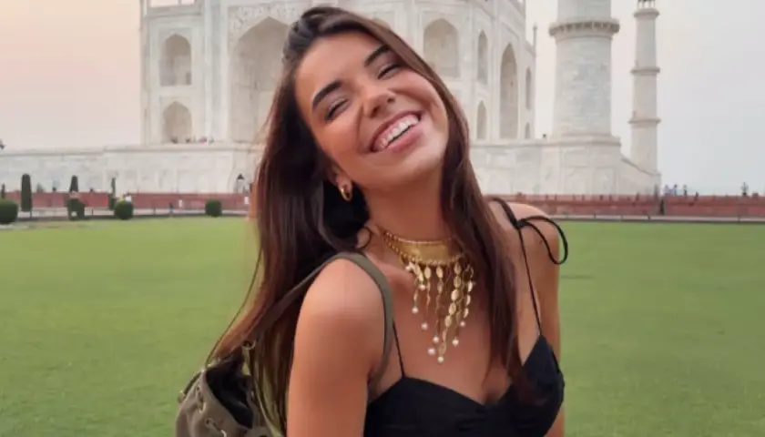 Elena Gortari sonríe feliz frente al Taj Mahal, luciendo un collar dorado y un vestido negro.