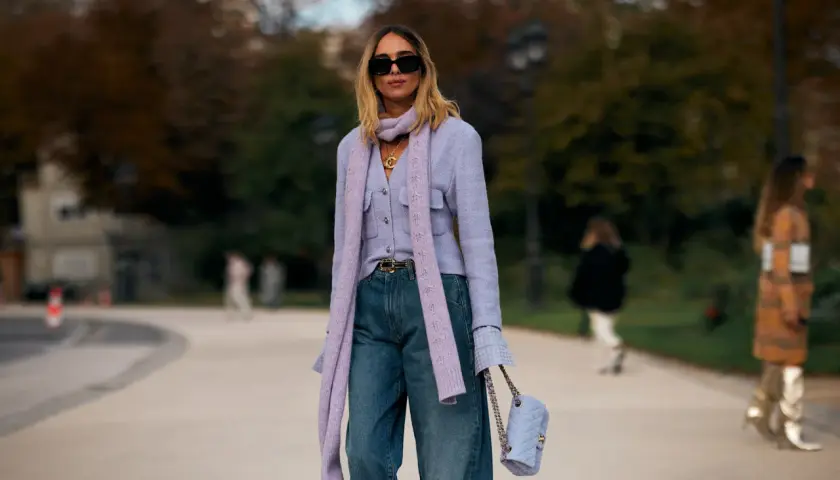 Mujer con look elegante con vaqueros, chaqueta lila, bufanda y bolso a juego.