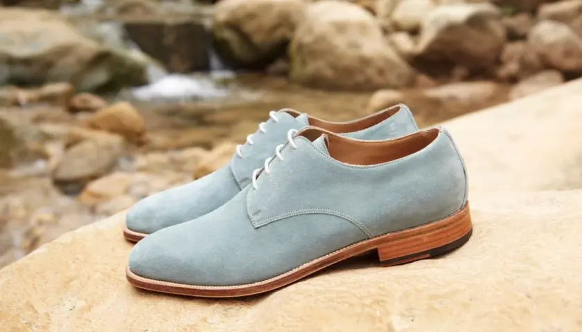 Zapatos de ante azul claro con cordones blancos, descansando sobre rocas junto a un arroyo. ¡Qué ante en zapatos!