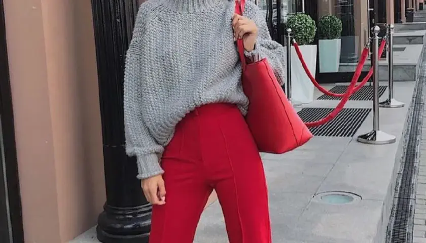 Chaqueta de punto gris y pantalones granate combinan a la perfección. Un bolso rojo vibrante completa el look.