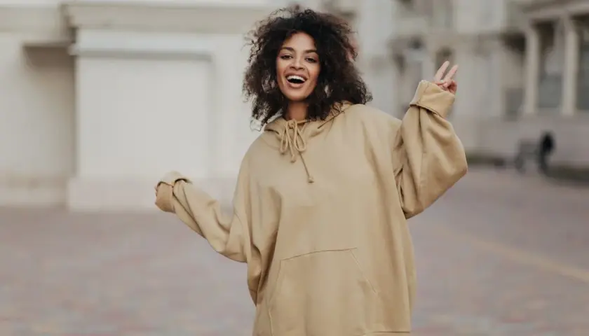 Mujer sonriente con pelo rizado, luciendo un cómodo estilo oversize en sudadera beige.