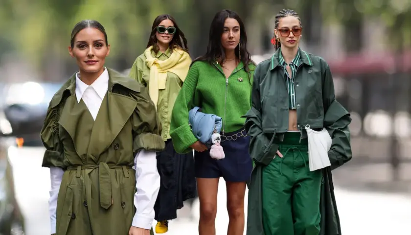Cuatro mujeres lucen atuendos en tonos de verde oscuro, desde gabardinas hasta chaquetas y pantalones, creando un look monocromático y elegante.