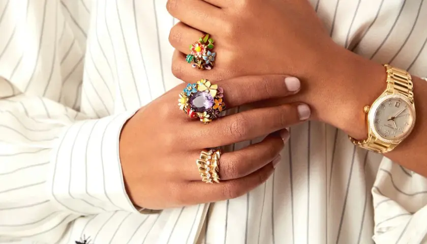 Manos adornadas con anillos florales coloridos y un reloj dorado, luciendo un estilo suot studio.