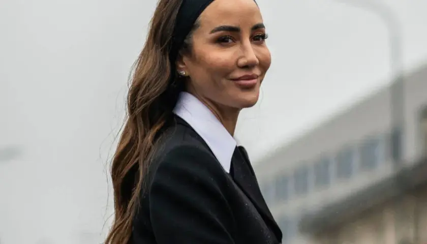Mujer con peinado con diadema y pelo suelto, luciendo un traje negro y camisa blanca.