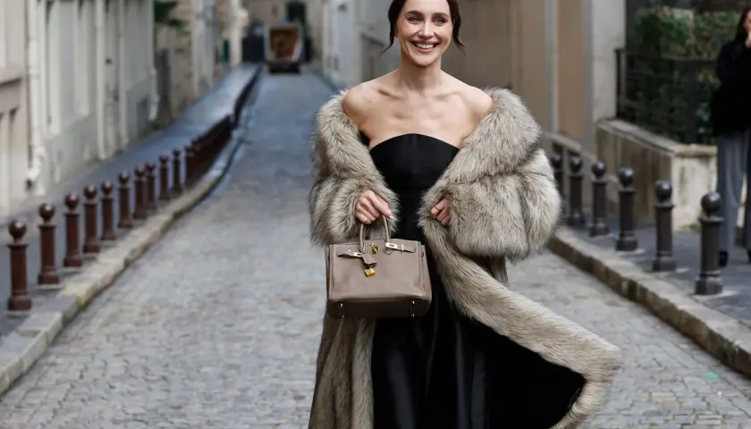 Elegante mujer con abrigo de pelo y bolso, lista para una boda en otoño.