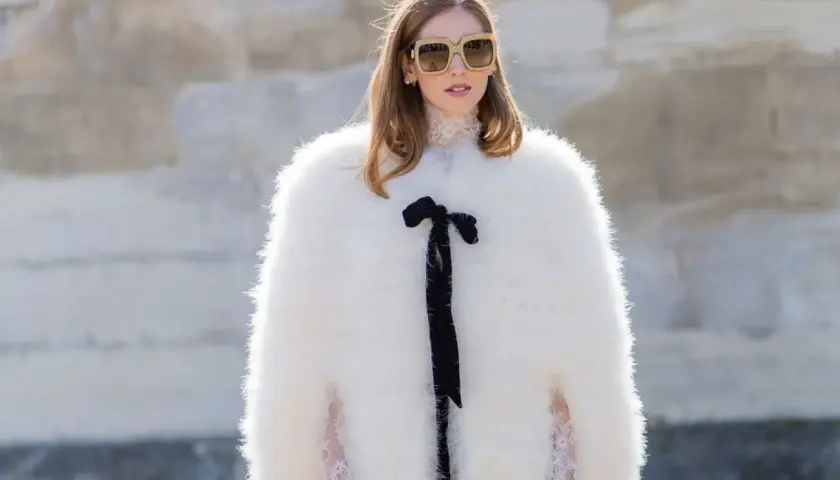 Estilo maximalismo: mujer con abrigo blanco de pelo, gafas grandes y lazo negro.